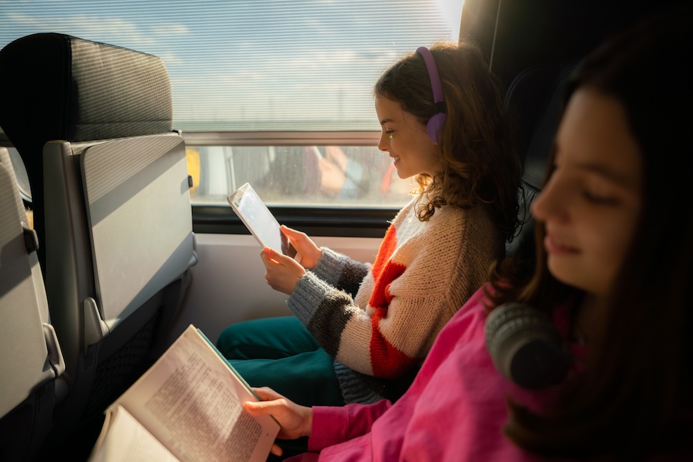 Kids travelling by train. Girls are reading a book and playing with tablets.