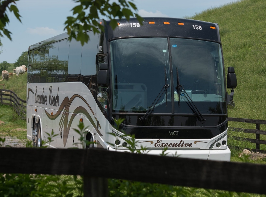 Executive Coach bus driving by a grassy field.